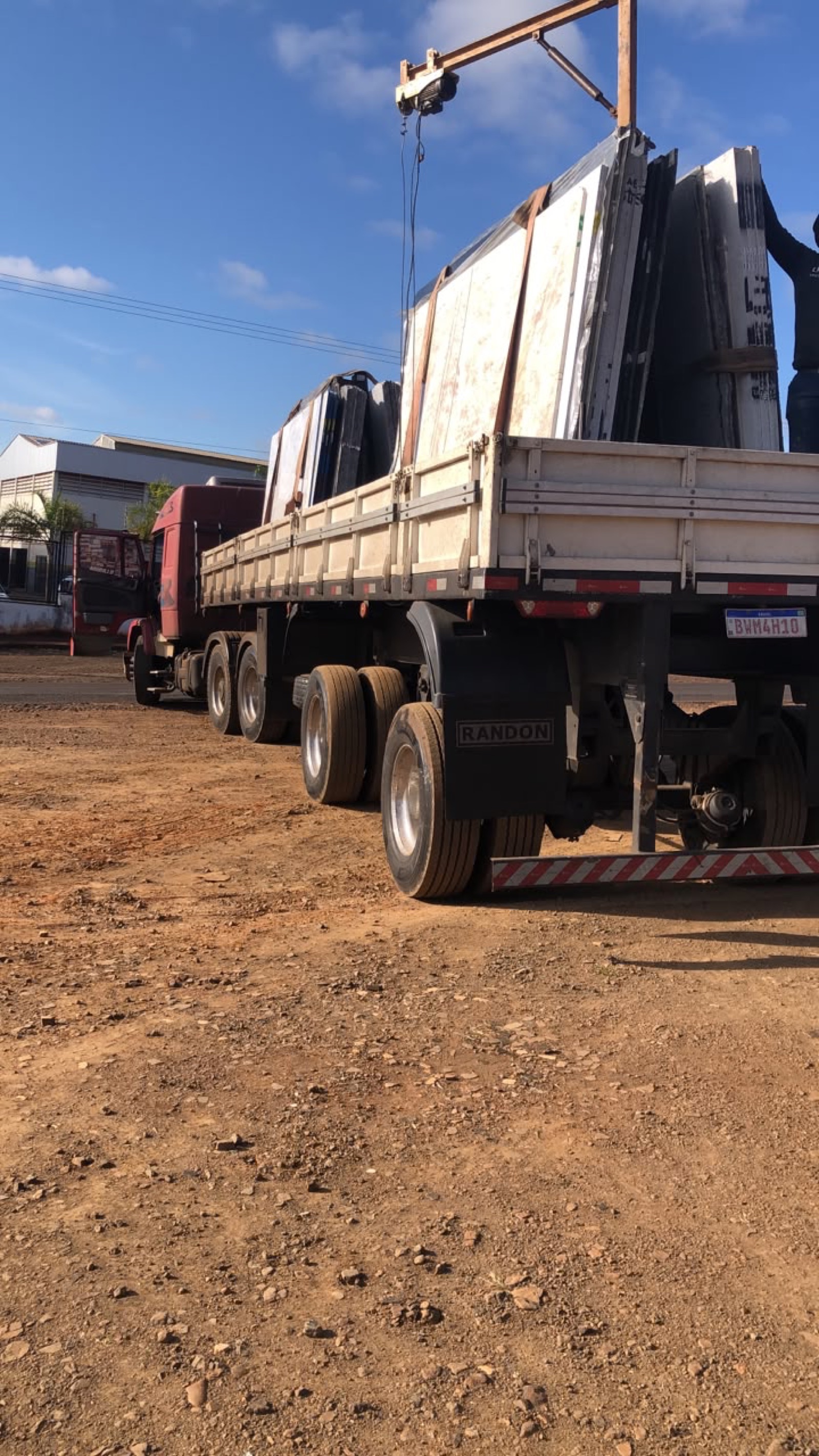 Carreta sendo carregada de chapas de granito com guindaste no pátio