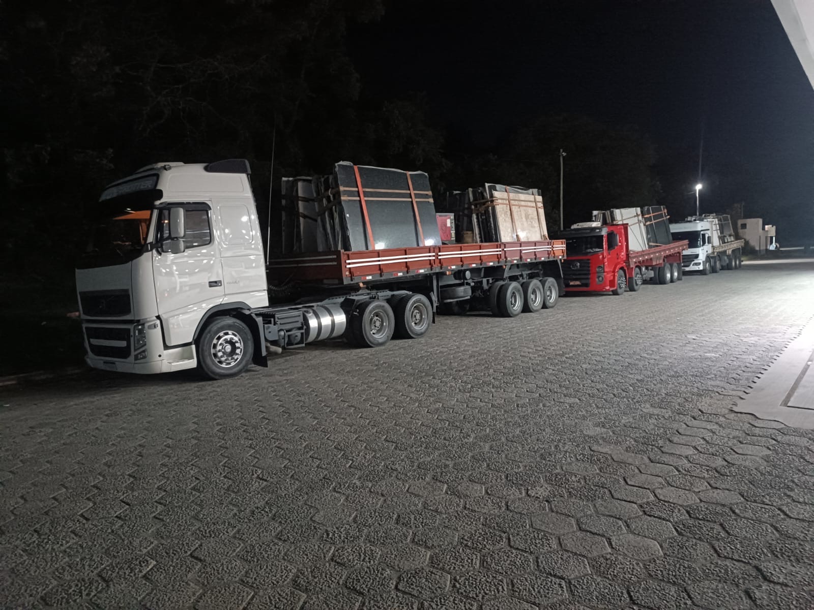 Comboio de carretas da TR Maizena carregadas de chapas de granito, à noite no pátio