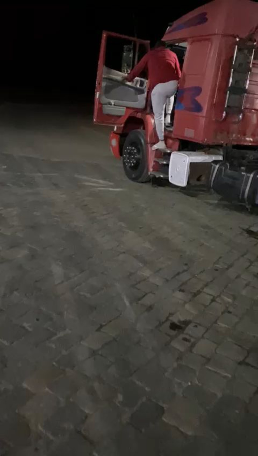 Caminhão no pátio à noite, motorista subindo na cabine